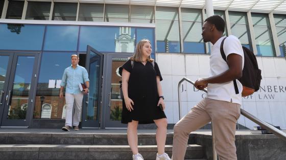 two students talking on stairs of college of law building and another law student in the background leaving the building